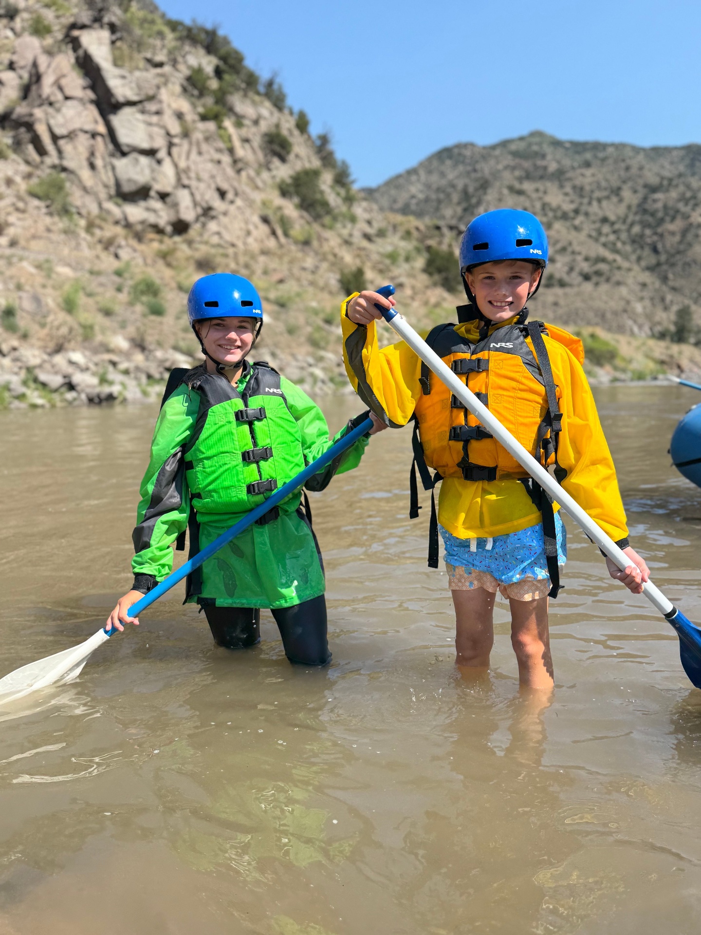 Two young Wolfpack rafters in helmets and PFDs standing in the Arkansas River