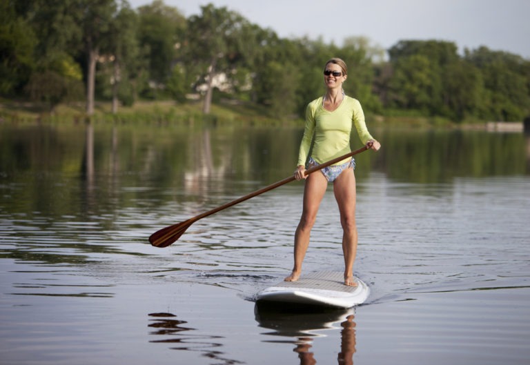 Stand Up Paddle Boarding Woman standing on a paddleboard on a calm Colorado lake, wearing a bright green rash guard and paddling on a sunny day
