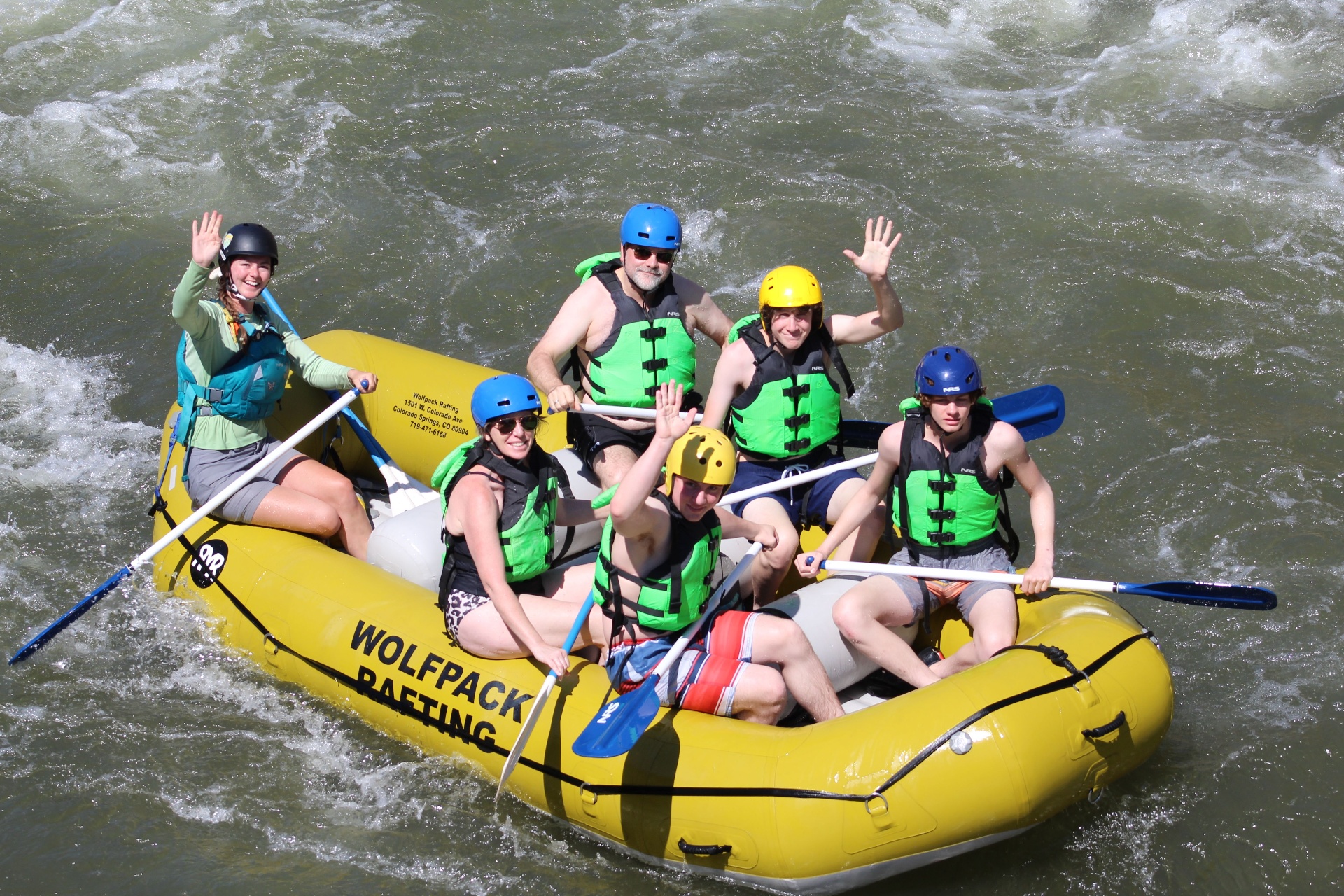 Wolfpack rafters waving from a yellow raft in the rapids
