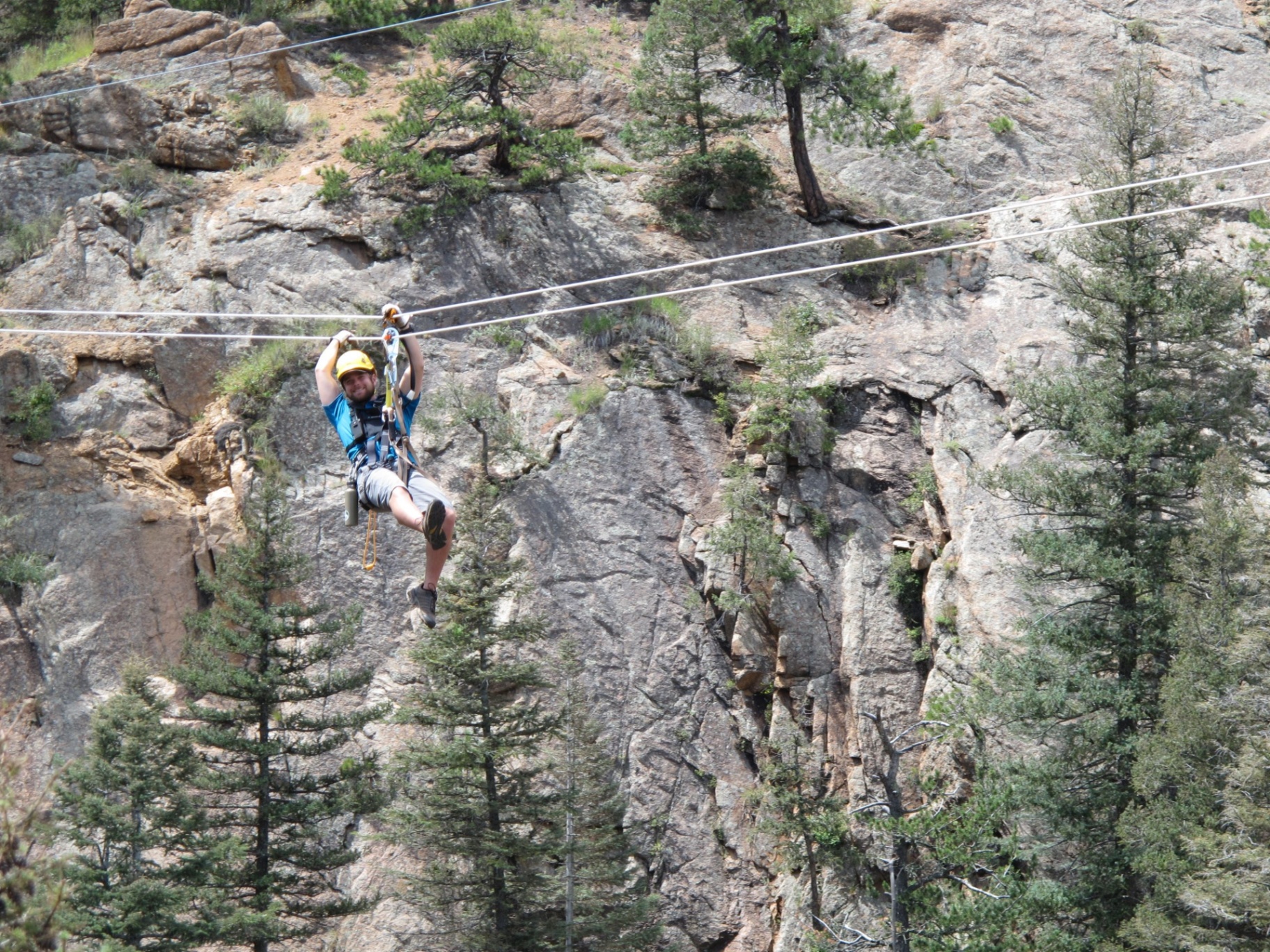 Seven Falls Zipline Tours Guest ziplining across a granite canyon lined with pine trees at Seven Falls in Colorado Springs